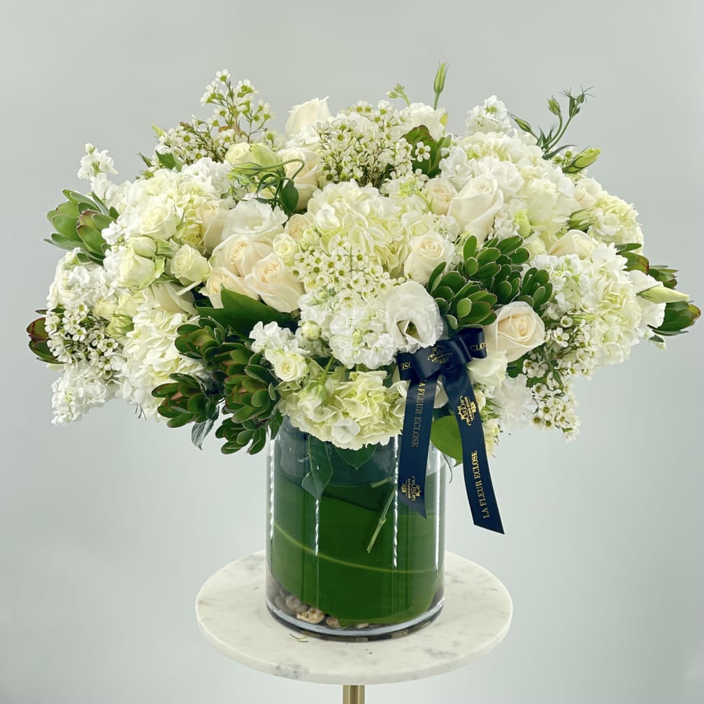 White floral arrangement in a glass vase with a navy ribbon