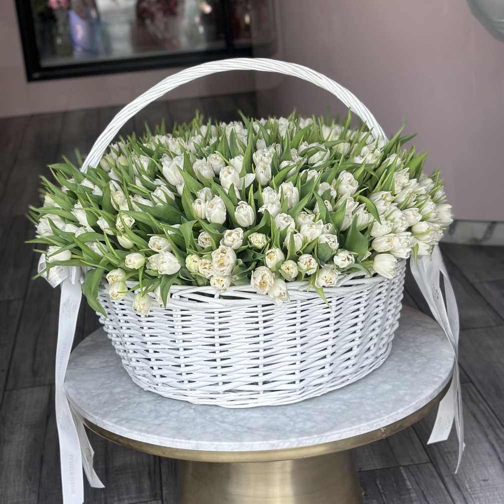 White tulips arranged in a white wicker basket with ribbon handles