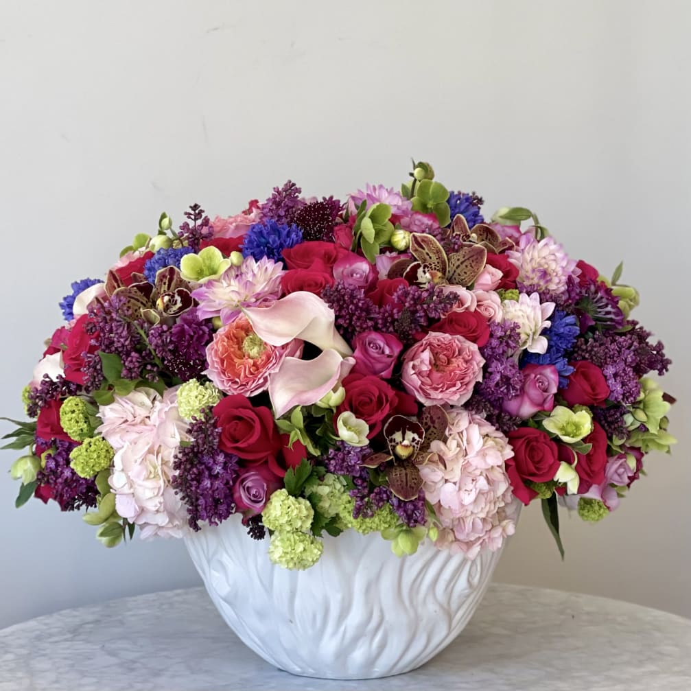 Large mixed bouquet in a white vase with pink, purple, and red blooms