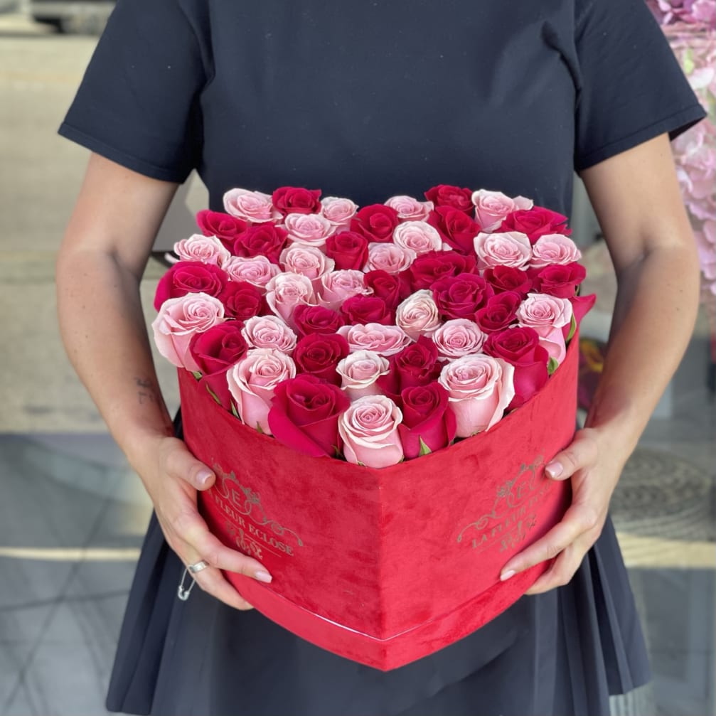Heart-shaped box of pink and red roses held by a person