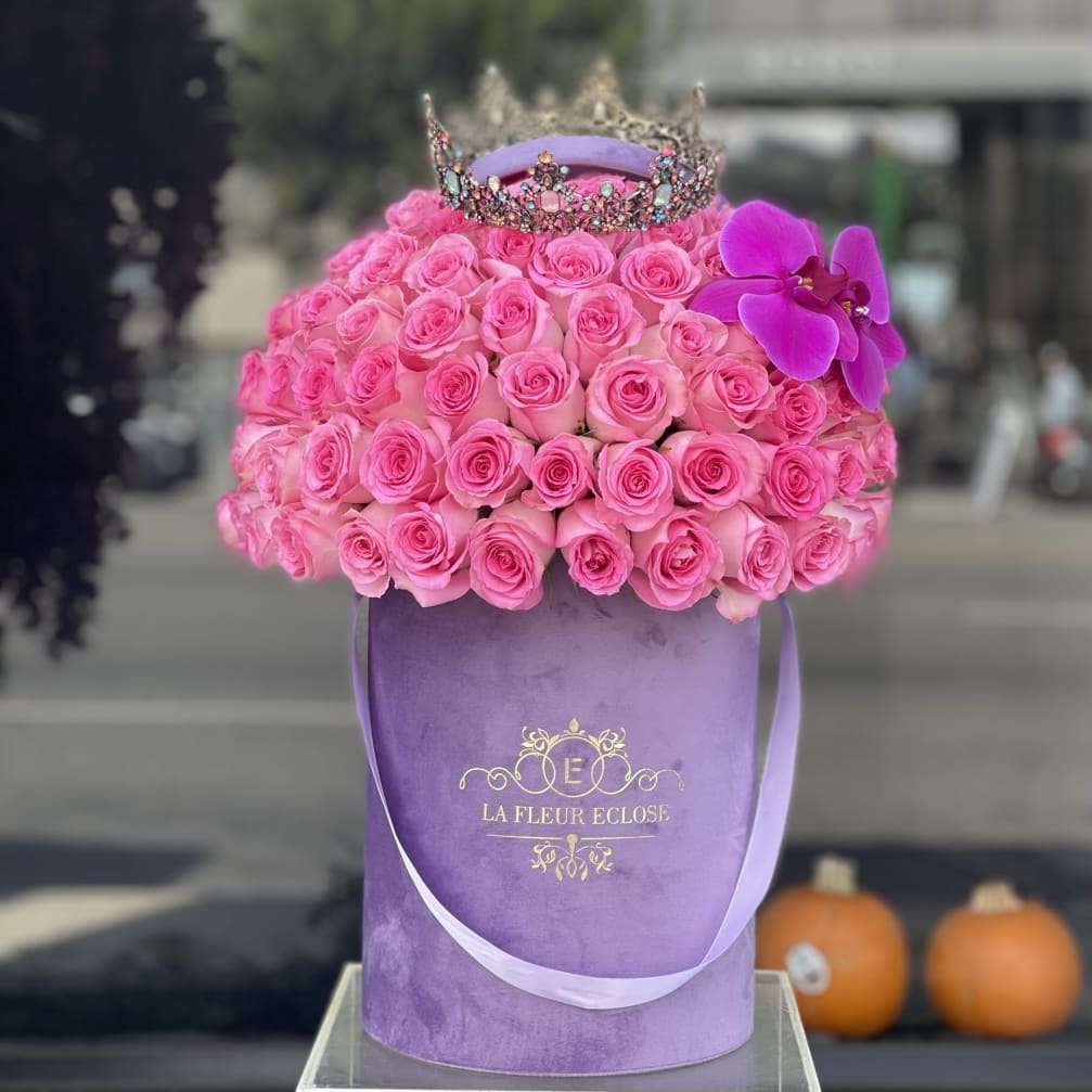 Pink roses in a purple hatbox with a jeweled crown and orchid accent