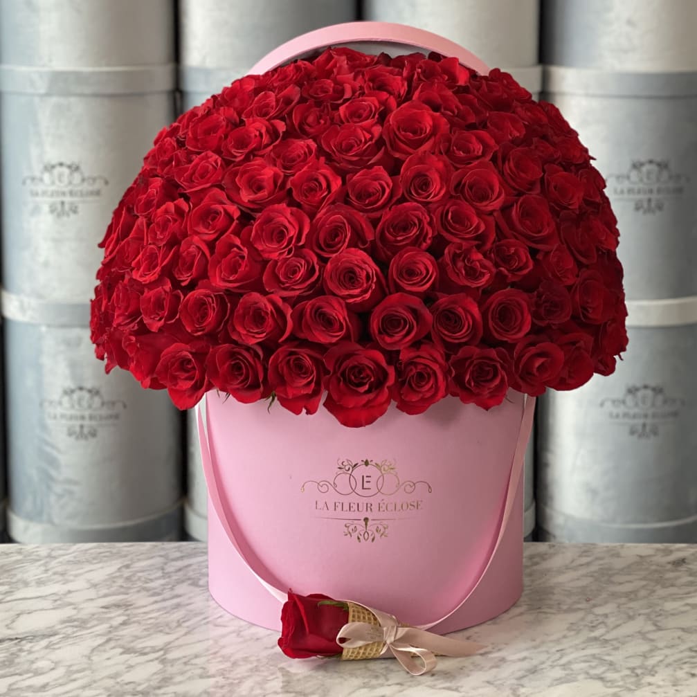 Large dome of red roses in a pink hatbox with a single rose at the base