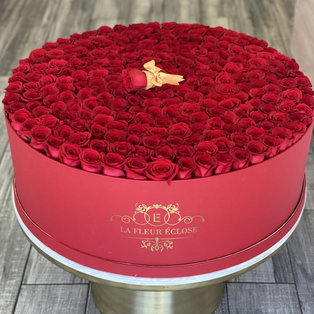 Round box filled with red roses and a single rose bud on top