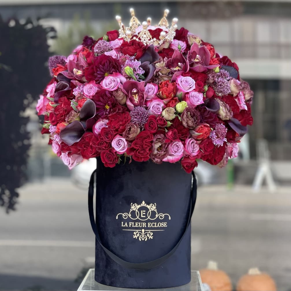 Large bouquet of red and pink roses in a black hatbox with a jeweled crown