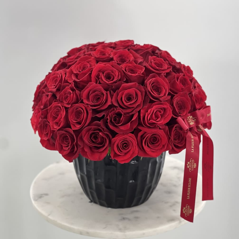 Round bouquet of red roses in a black vase with a red ribbon