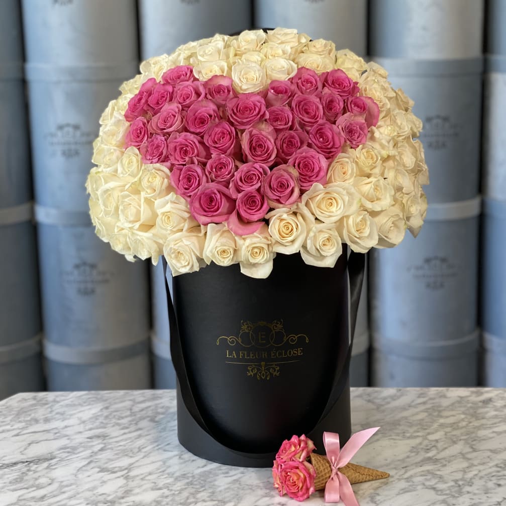 Pink and cream roses arranged in a black hat box with a small rose cone accent