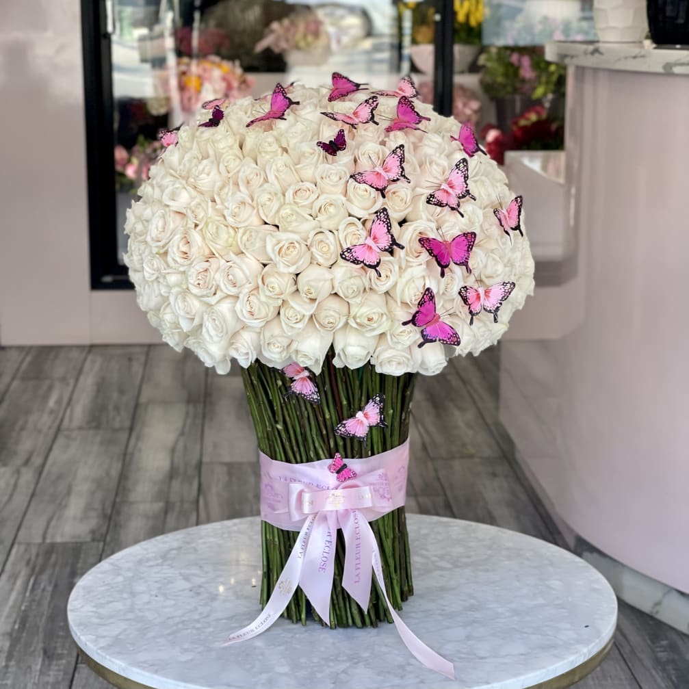 Large bouquet of white roses with pink butterfly accents and a pink ribbon