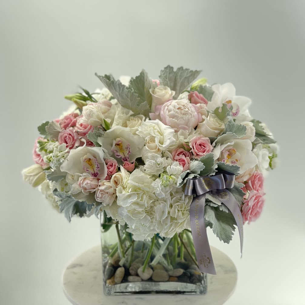 Pink and white floral arrangement in a square glass vase with a ribbon