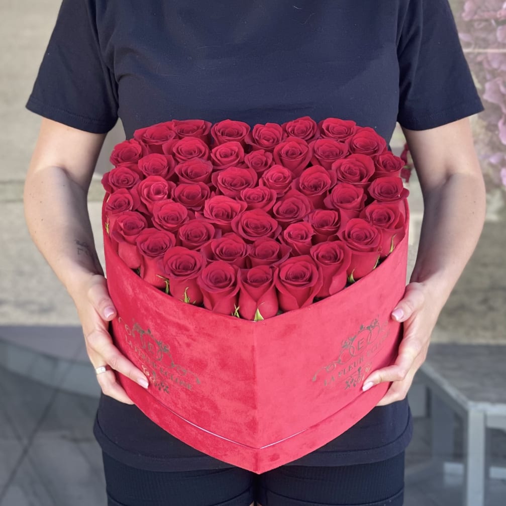 Heart-shaped box filled with red roses being held by a person