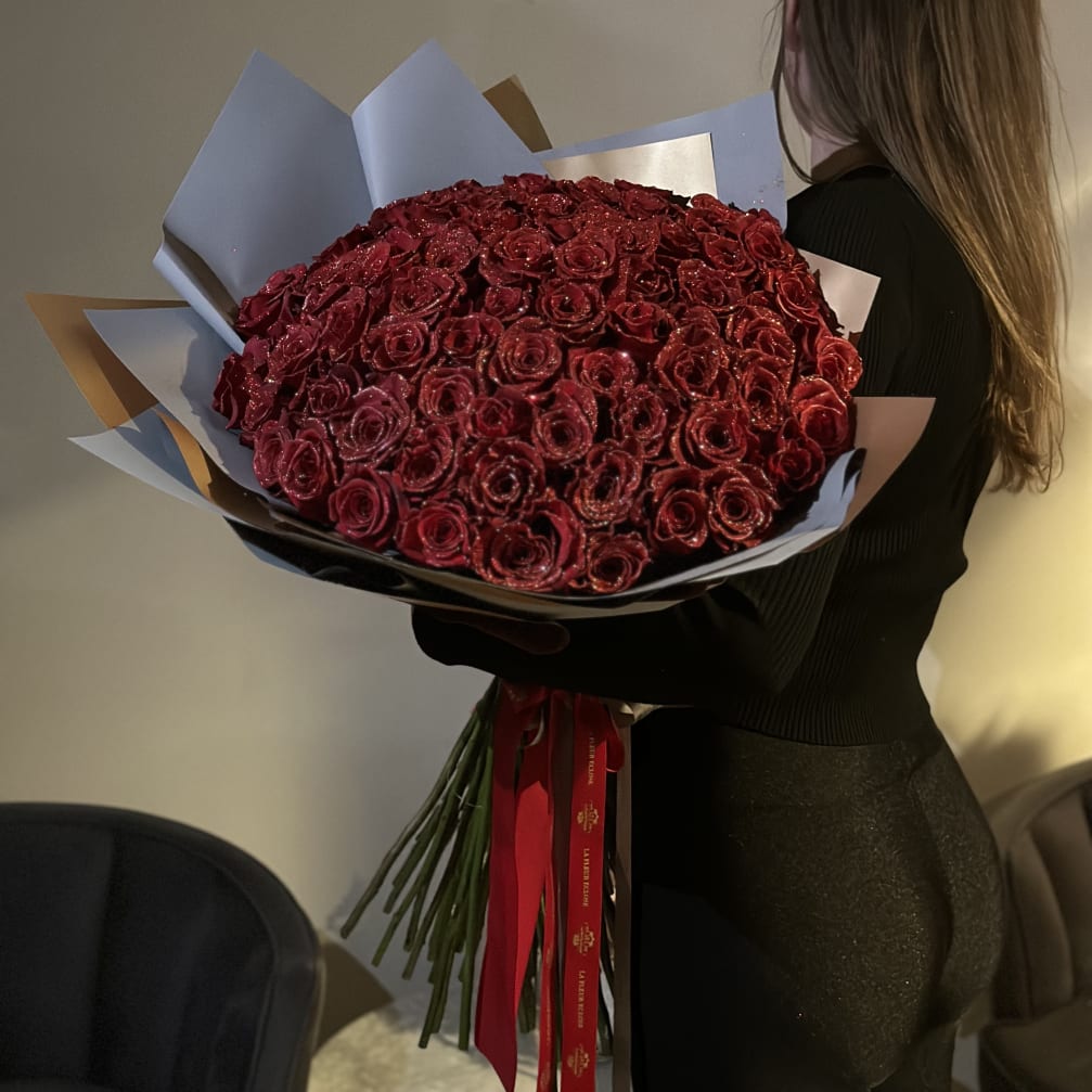 Woman holding a large bouquet of red roses wrapped in paper