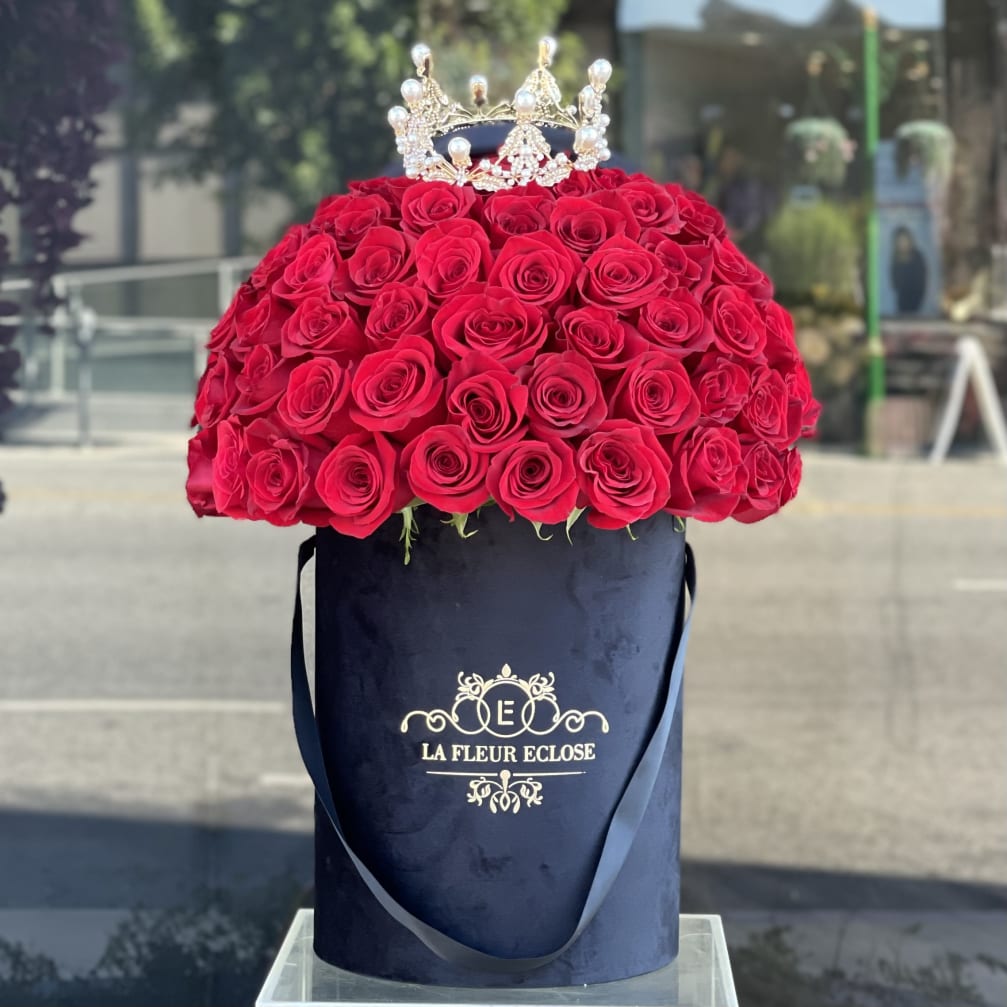 Red rose arrangement in a navy hat box with a jeweled crown topper