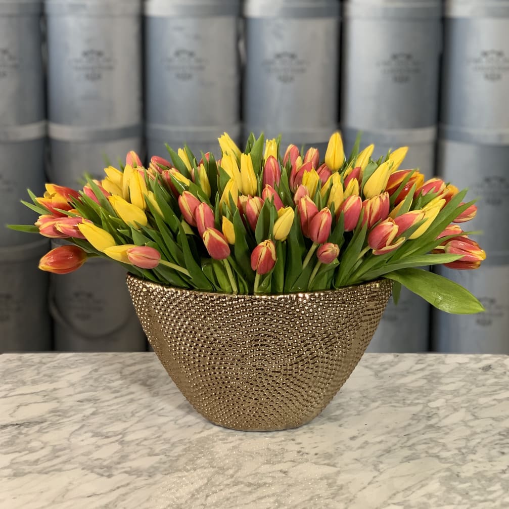 Yellow and pink tulips arranged in a gold textured vase