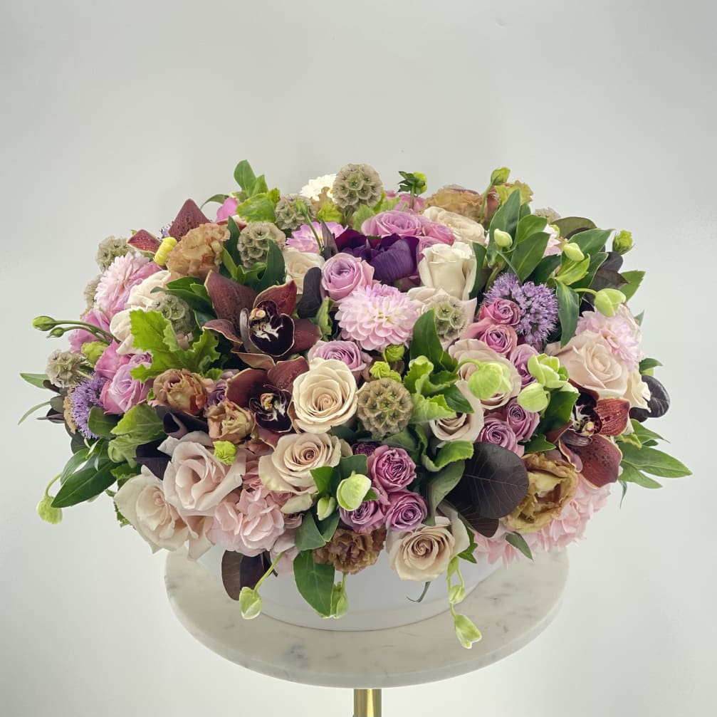 Large pastel bouquet with roses, orchids, and pink blooms in a white container