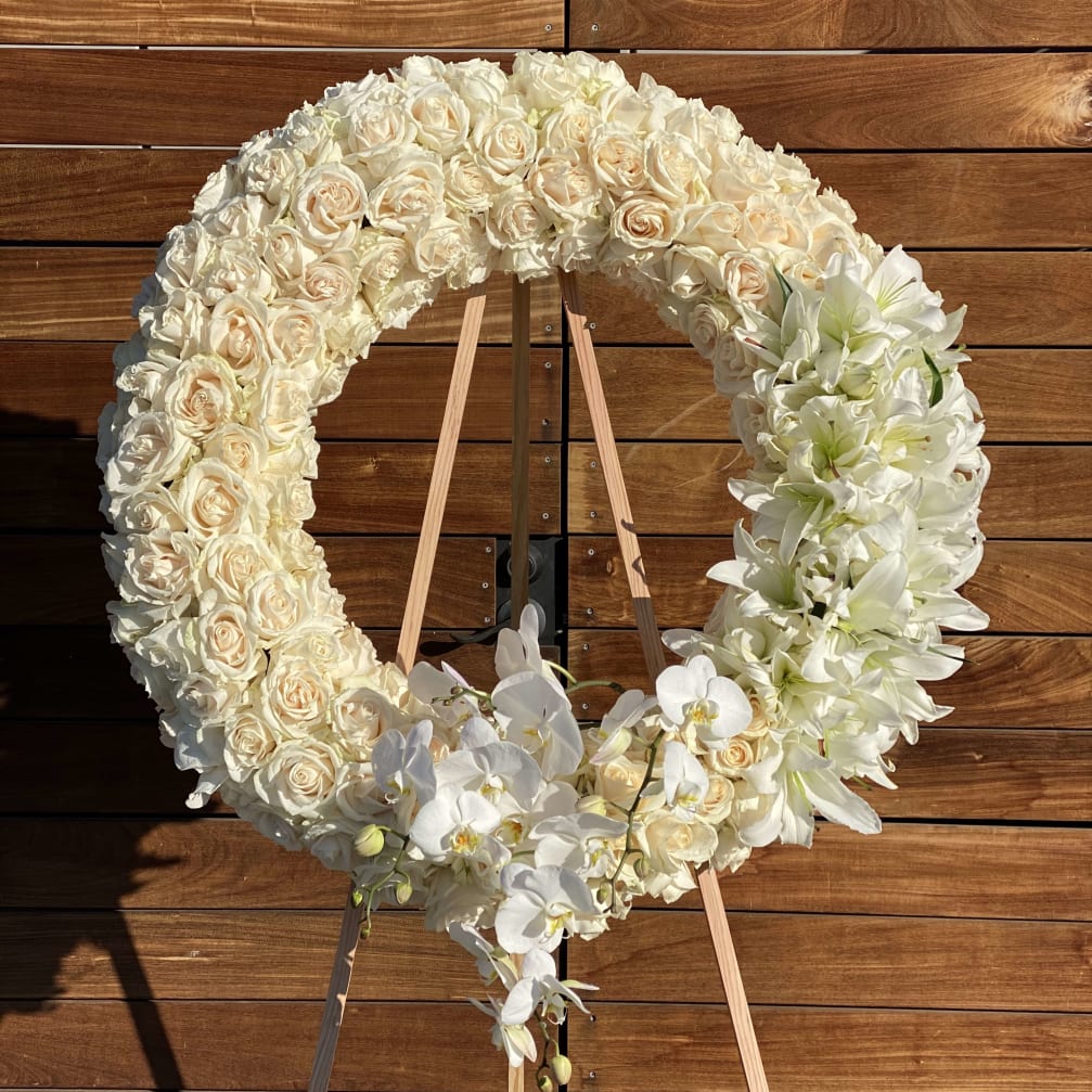 Cream rose and white orchid floral wreath on a wooden stand