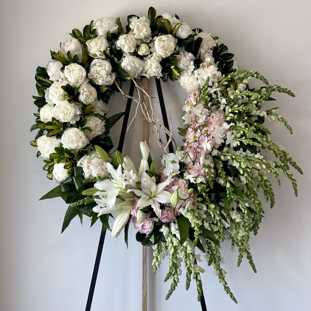 Large floral wreath with white blooms, lilies, and pink accents on a stand