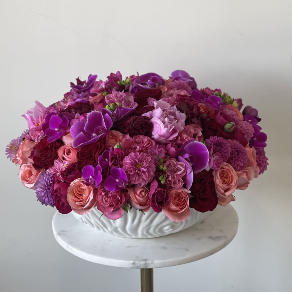 Round arrangement of pink and purple flowers in a white bowl vase