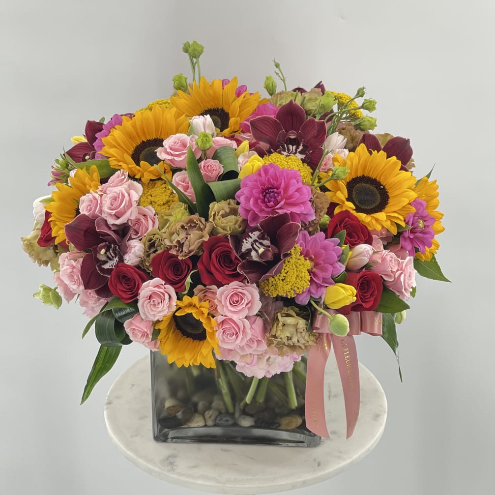 Mixed bouquet with sunflowers, roses, and orchids in a square glass vase