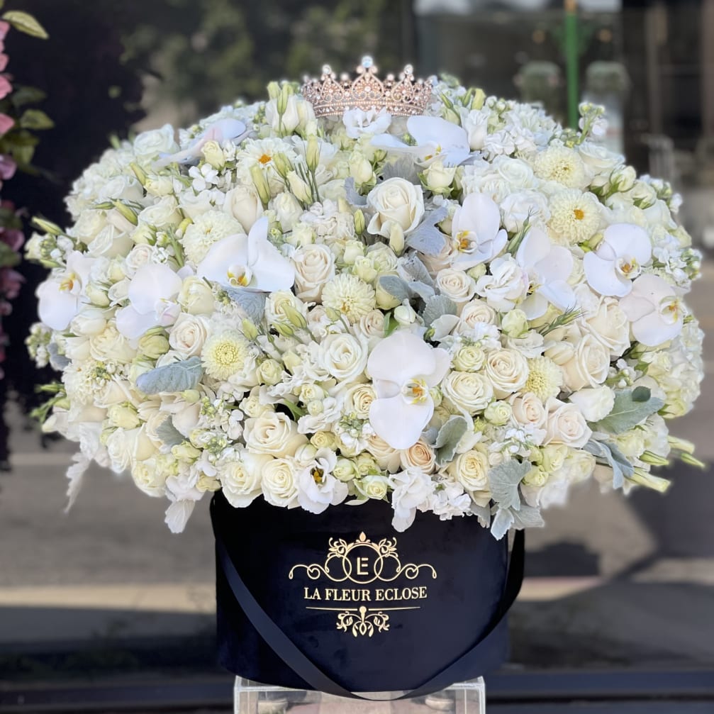 Large white floral arrangement in a black hat box with a tiara on top.