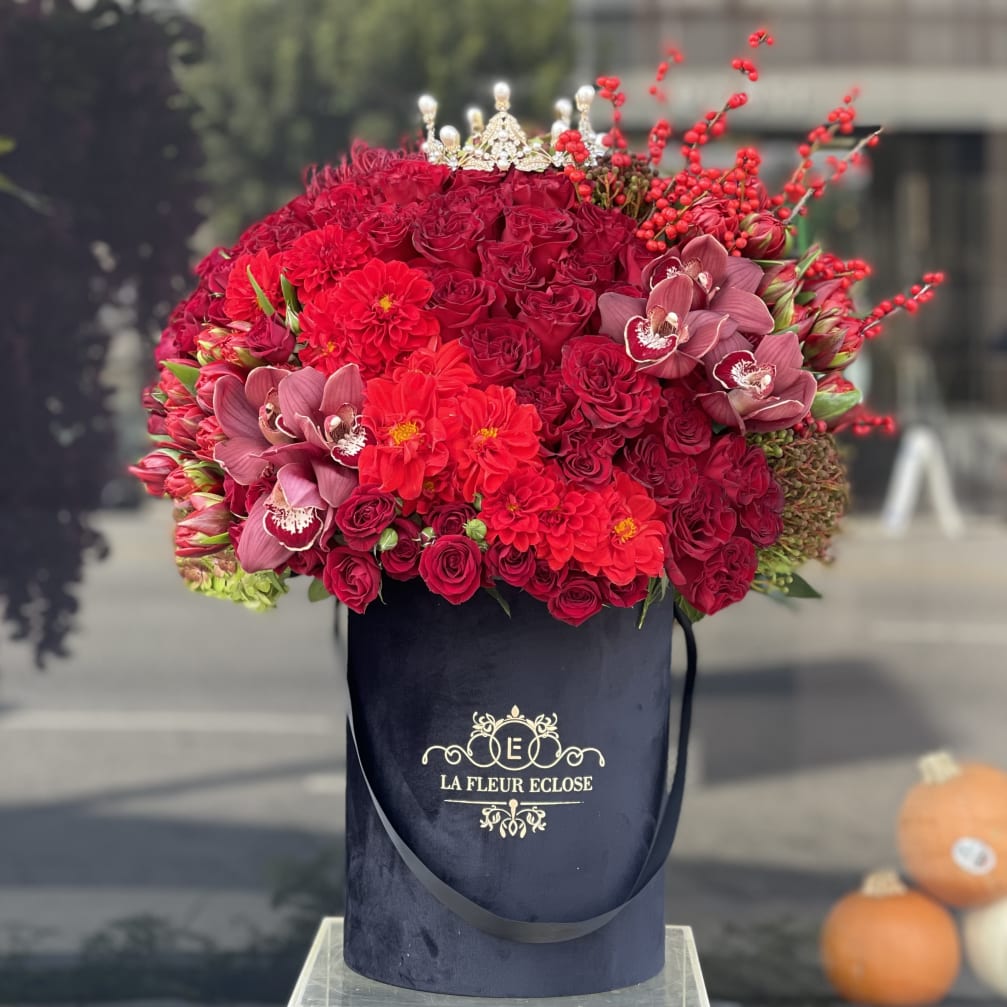 Large red floral arrangement in a black hatbox with orchids and roses