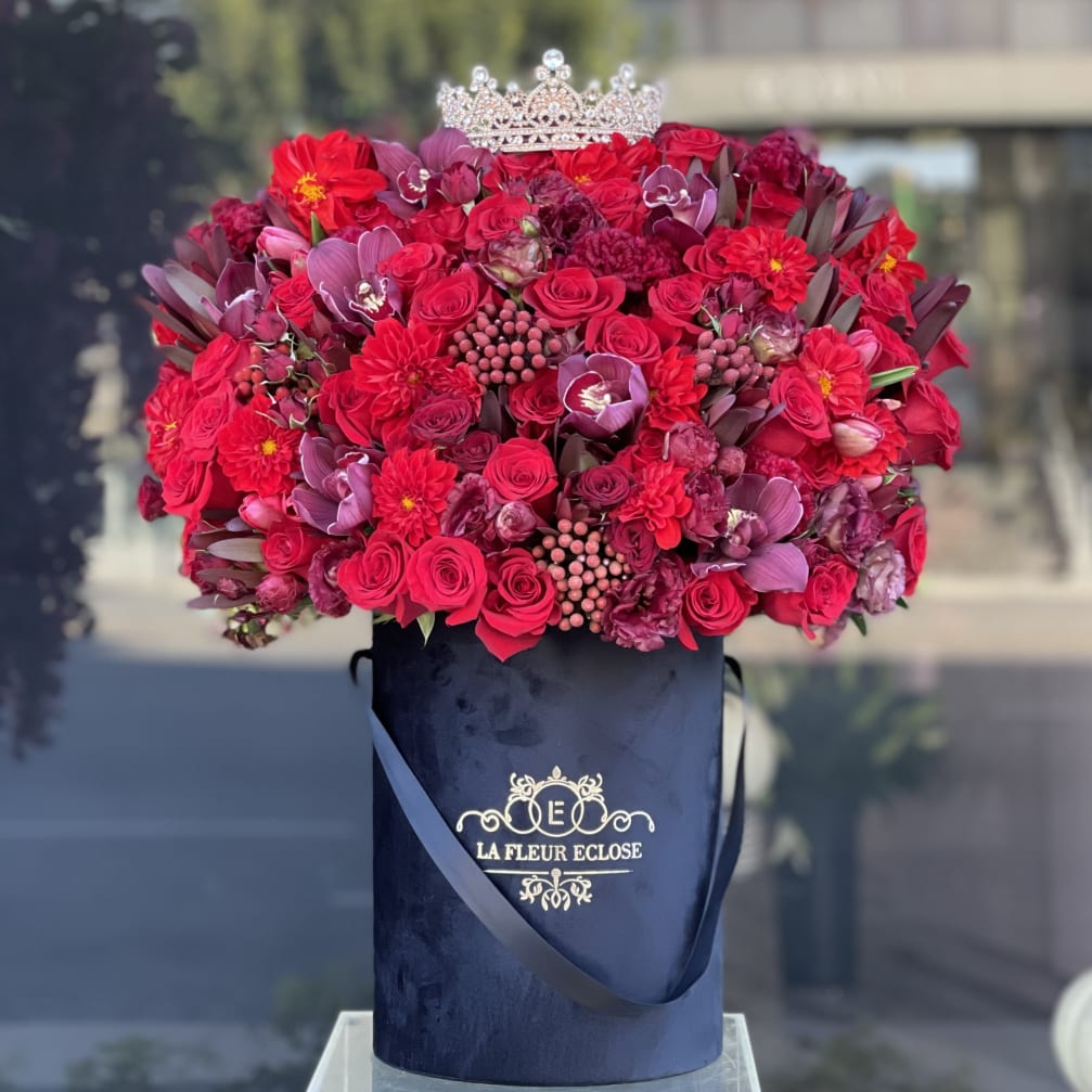 Red and purple bouquet in a navy hatbox with a jeweled crown topper
