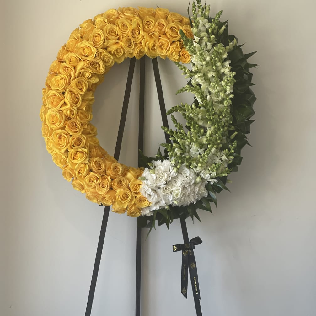 Yellow rose wreath on a black easel with white flowers and greenery
