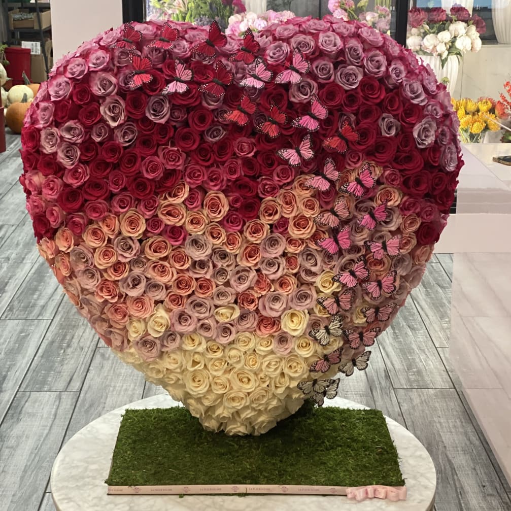 Heart-shaped rose arrangement with pink butterflies on a grass-covered base