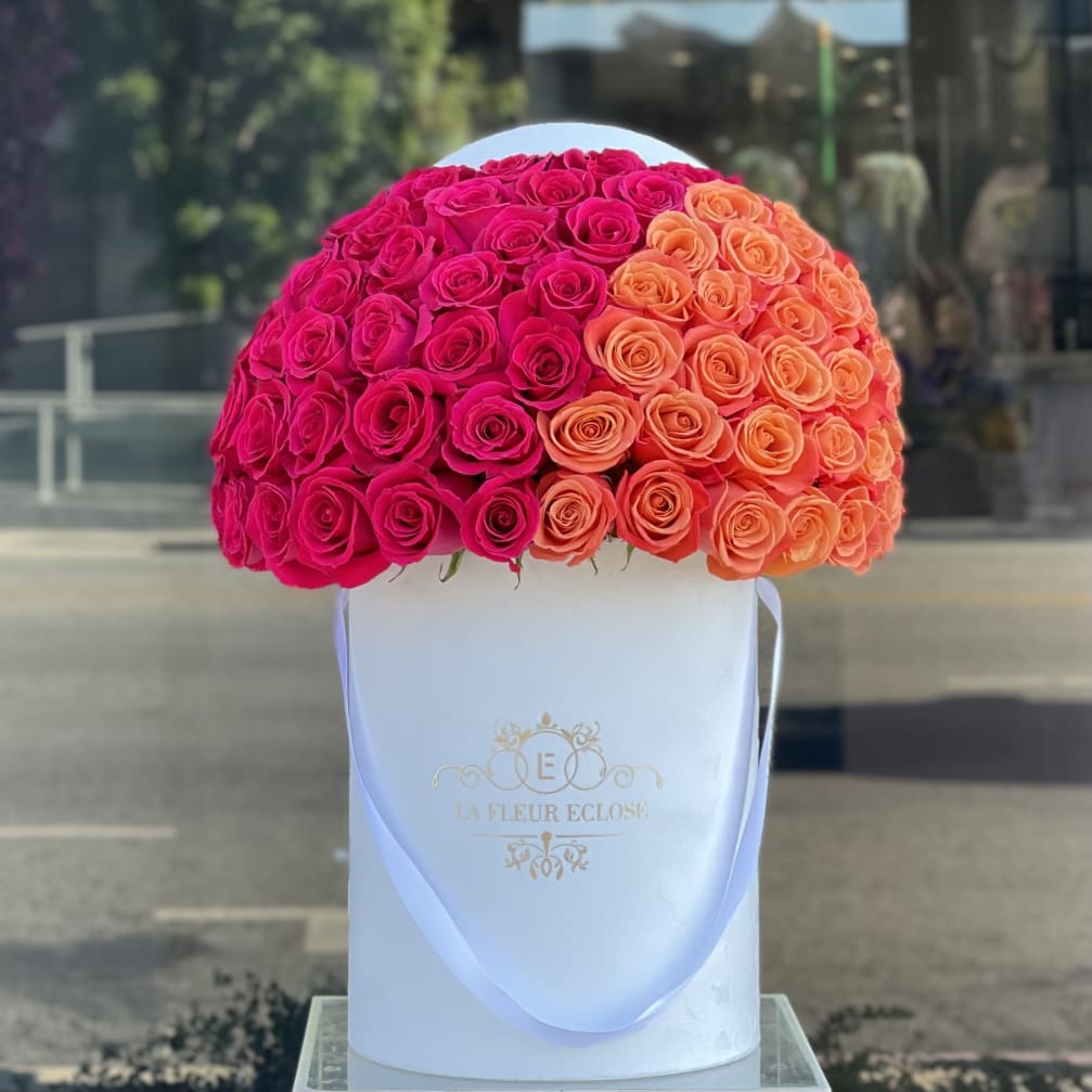 Round rose arrangement in a white hat box with pink and orange blooms