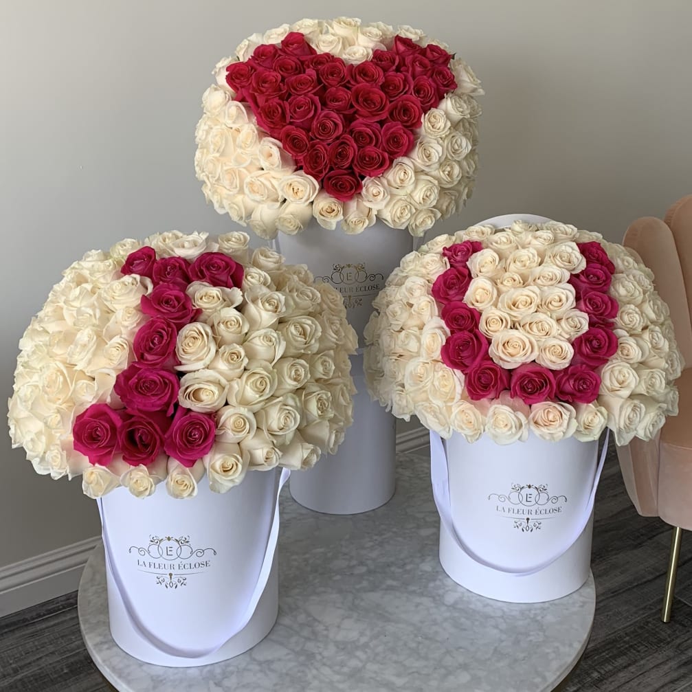 Three round rose arrangements in white boxes, two with pink heart designs