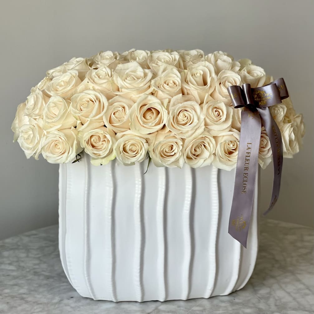 Cream rose arrangement in a white ribbed vase with a ribbon bow