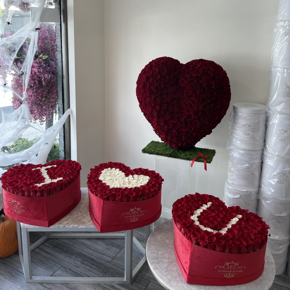Heart-shaped red rose arrangements in pink boxes and on a stand