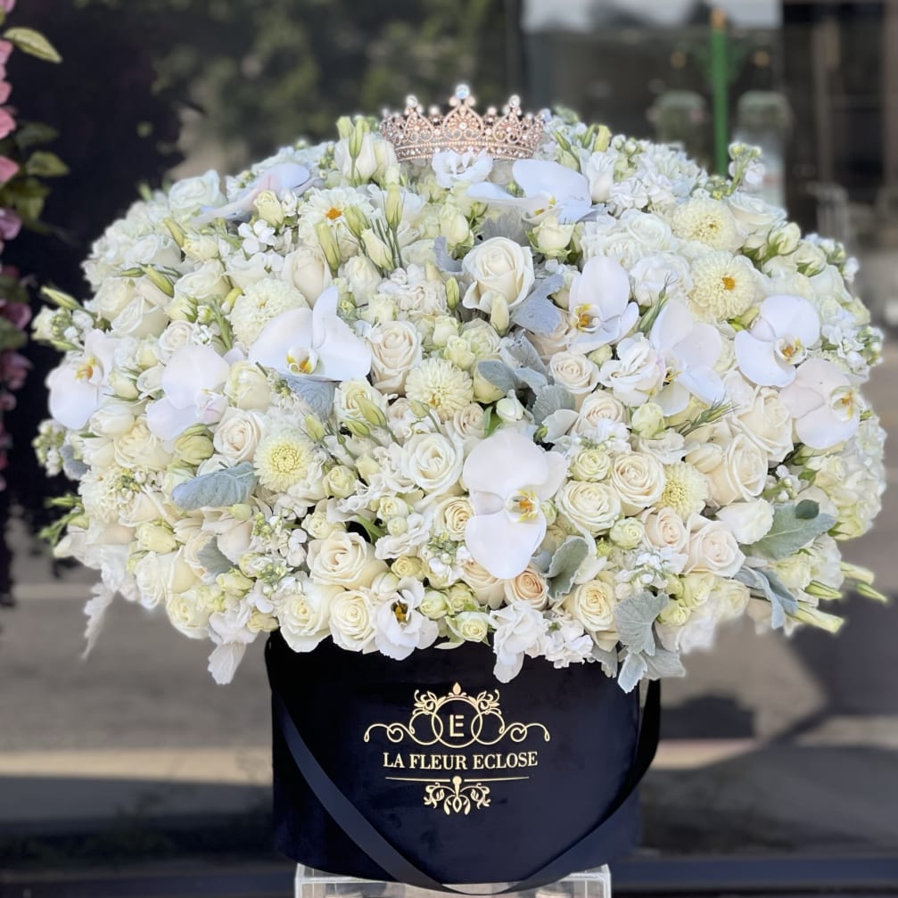 Large white floral arrangement in a black hatbox with a crown topper