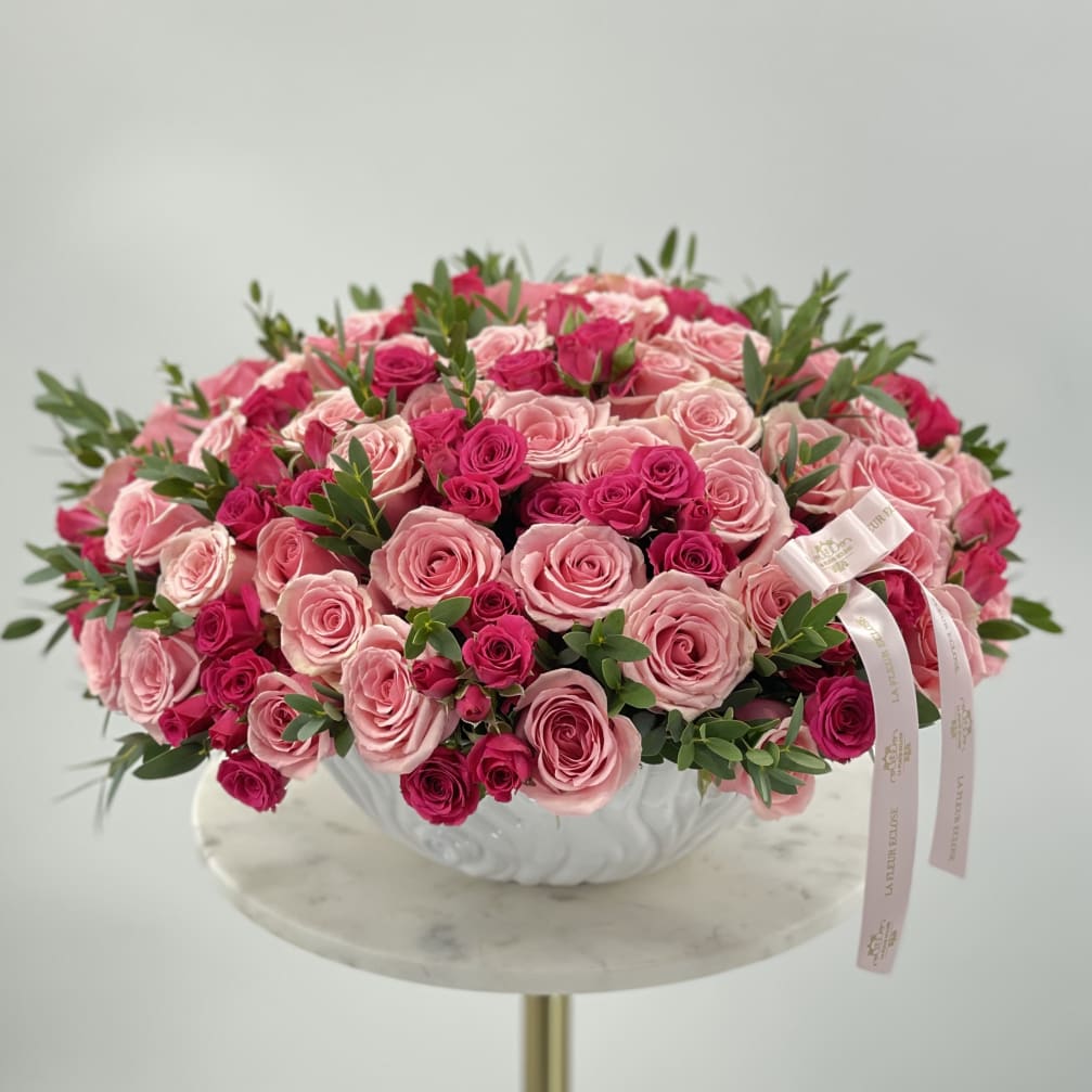 Pink and hot pink roses arranged in a white bowl vase