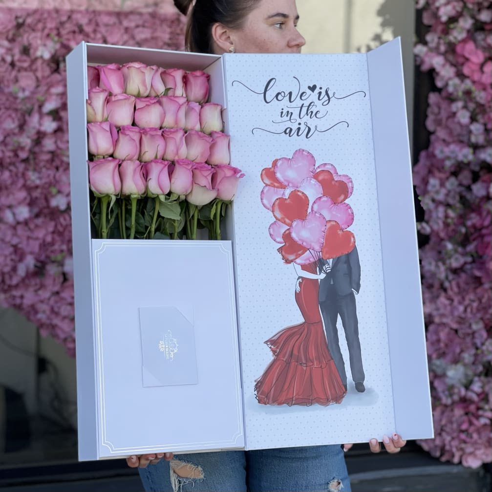 Box of pink roses with a love-themed card and heart balloons