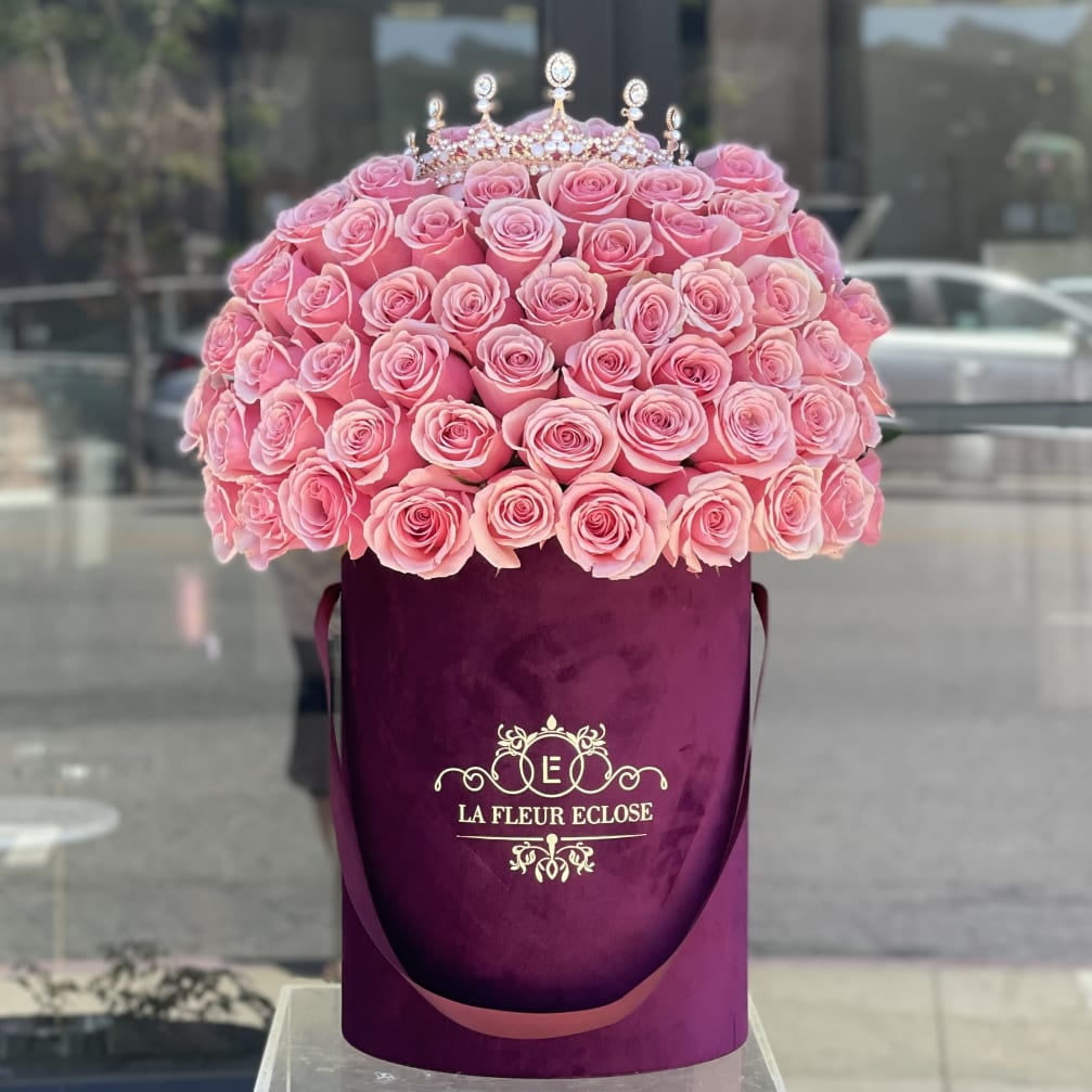 Pink roses arranged in a purple hatbox with a jeweled crown topper