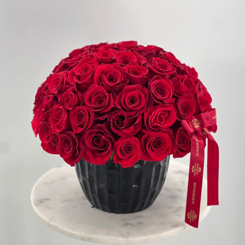 Round bouquet of red roses in a black vase with a red ribbon