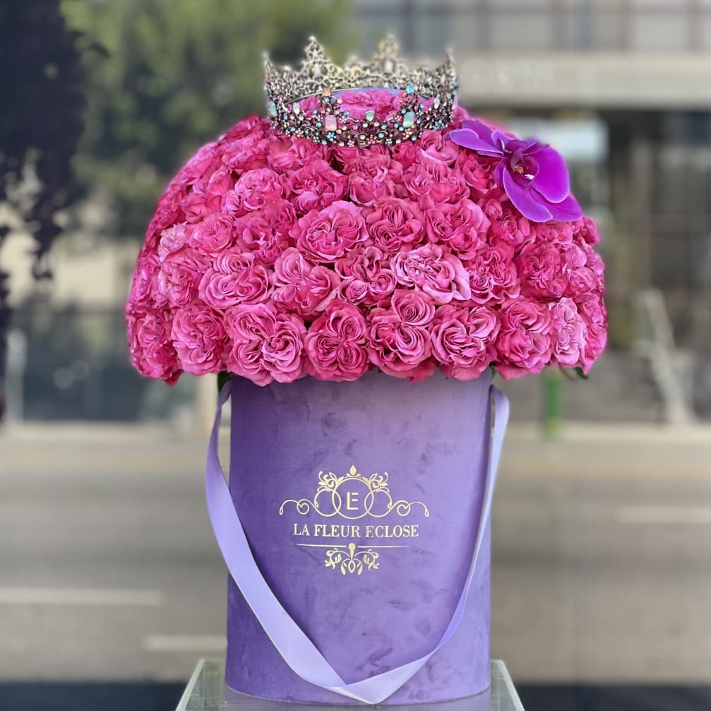 Pink rose arrangement in a purple hatbox with a jeweled crown