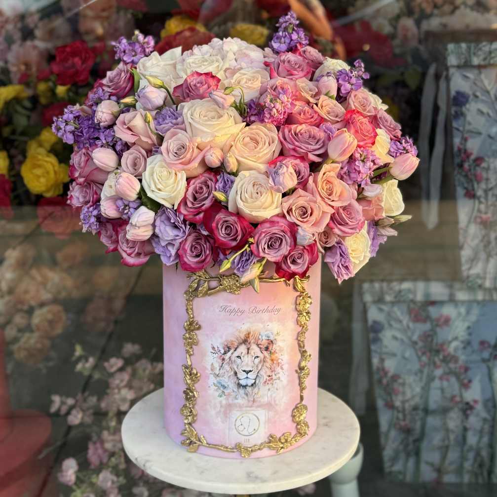 Pink and lavender roses arranged in a tall pink box with a lion illustration
