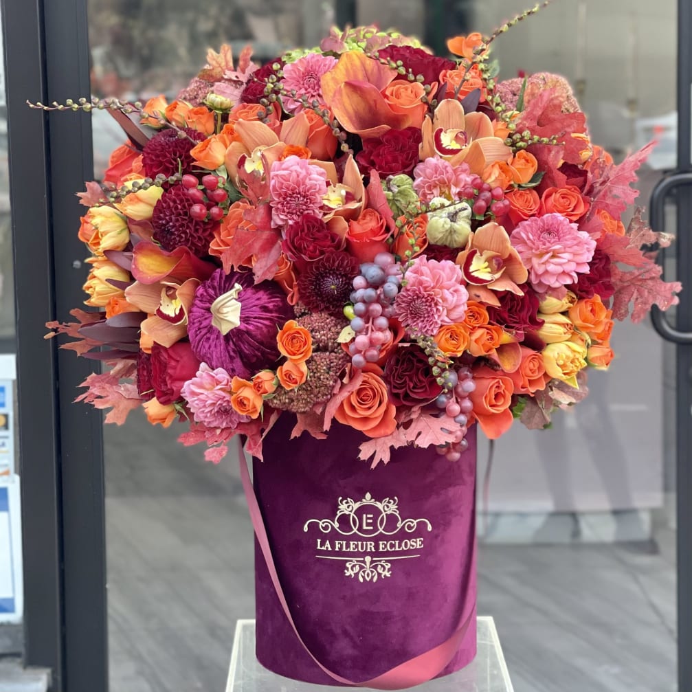 Large bouquet of orange, pink, and red flowers in a purple hatbox