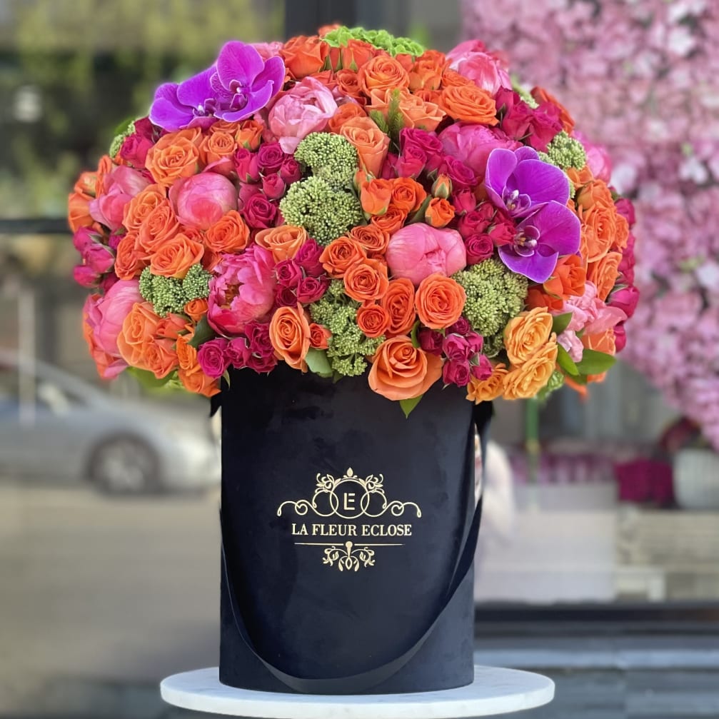 Large bouquet of orange, pink, and purple flowers in a black hatbox