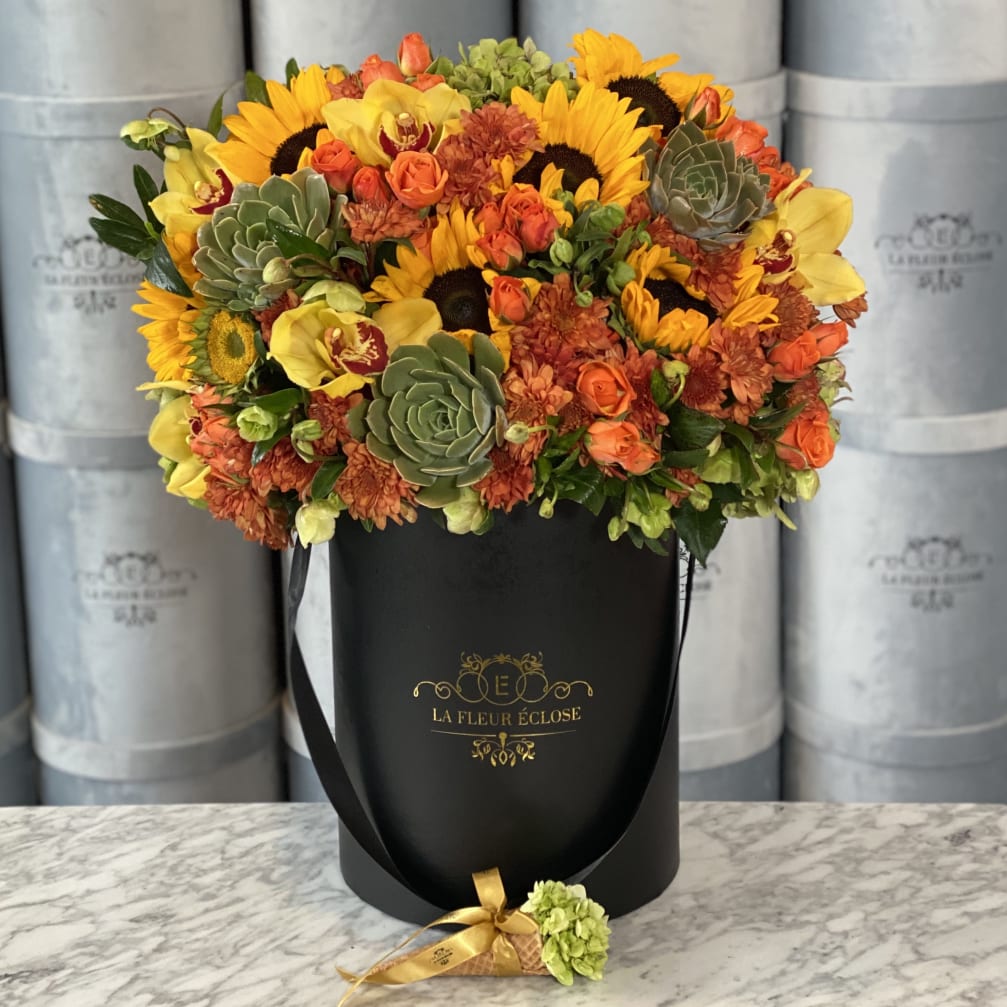 Bouquet of sunflowers, orange roses, and succulents in a black hatbox