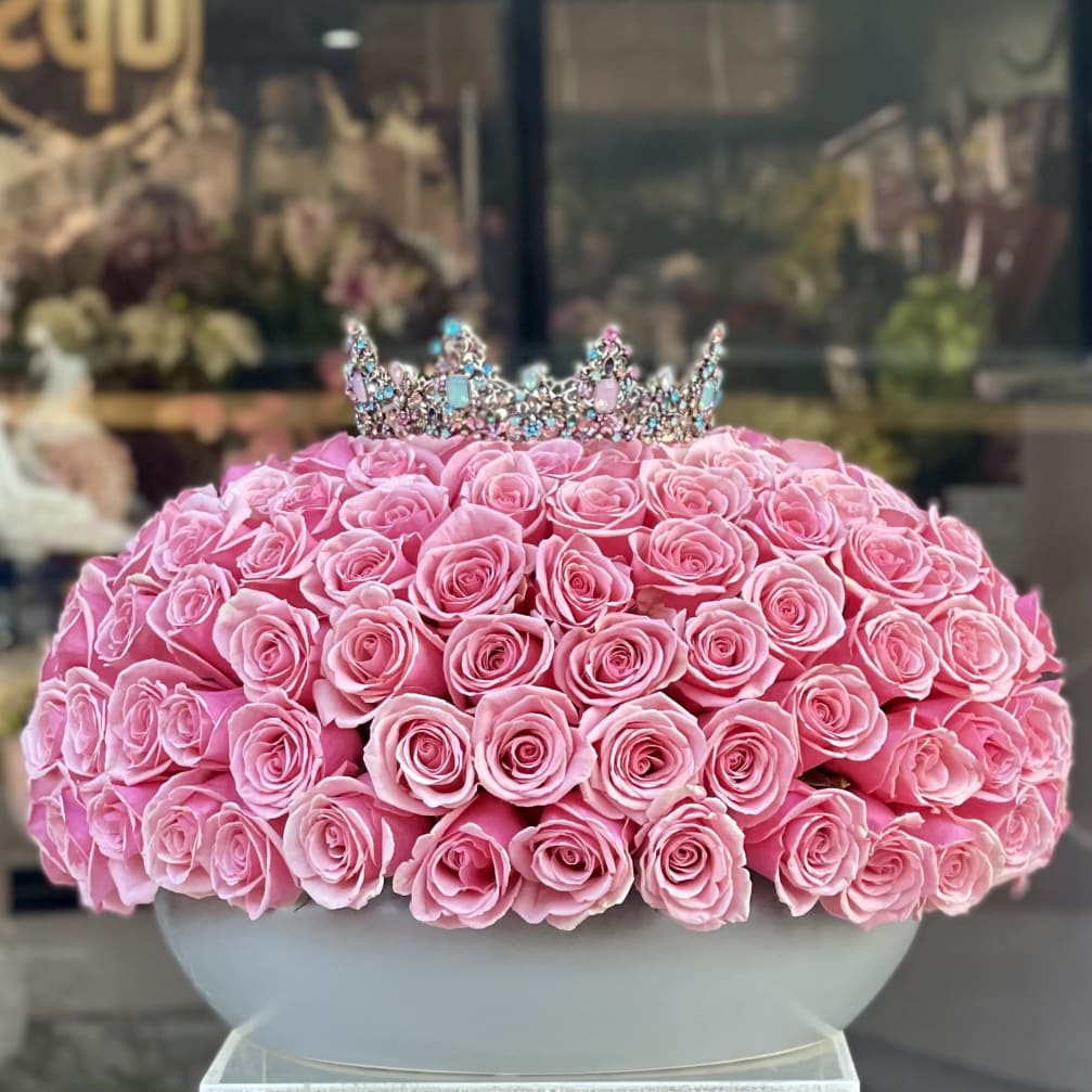Pink rose arrangement topped with a jeweled crown in a white bowl vase