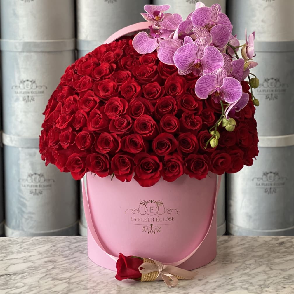 Red rose arrangement in a pink hatbox with pink orchids and a single rose