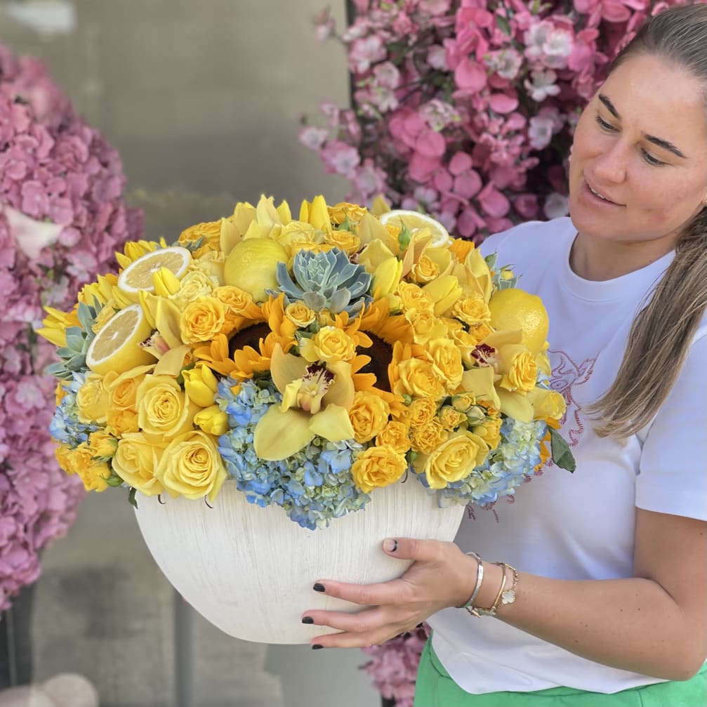 Woman holding a large yellow floral arrangement in a white bowl vase