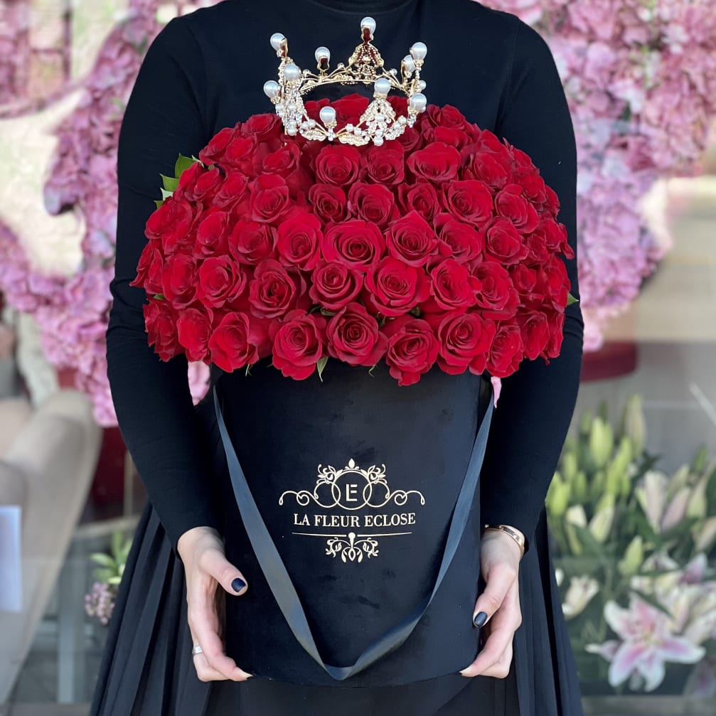 Large red rose arrangement in a black hatbox with a jeweled crown topper
