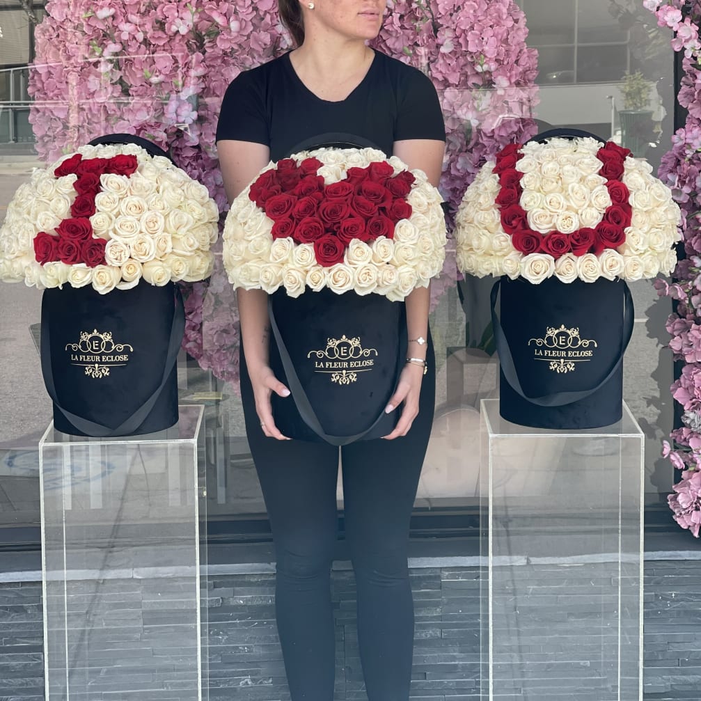 Three large rose arrangements in black hat boxes, with red roses forming letters.