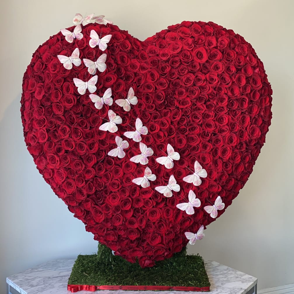 Heart-shaped red rose arrangement with white butterflies on a base