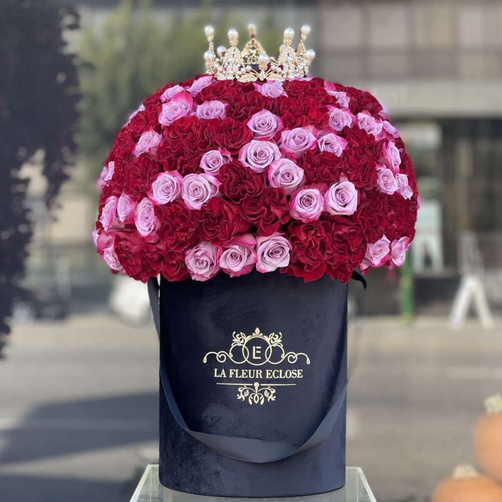 Red and pink roses arranged in a black hat box with a crown topper