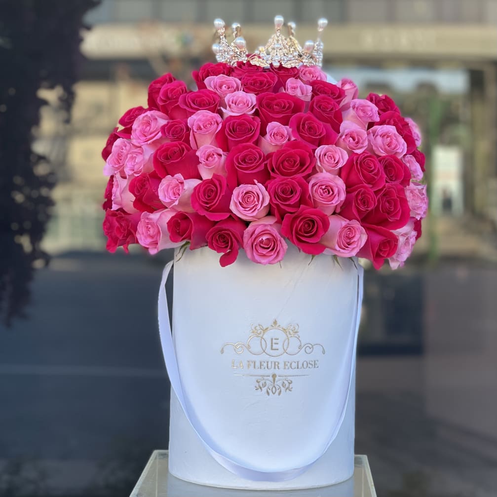 Pink and red roses arranged in a white hat box with a small crown topper