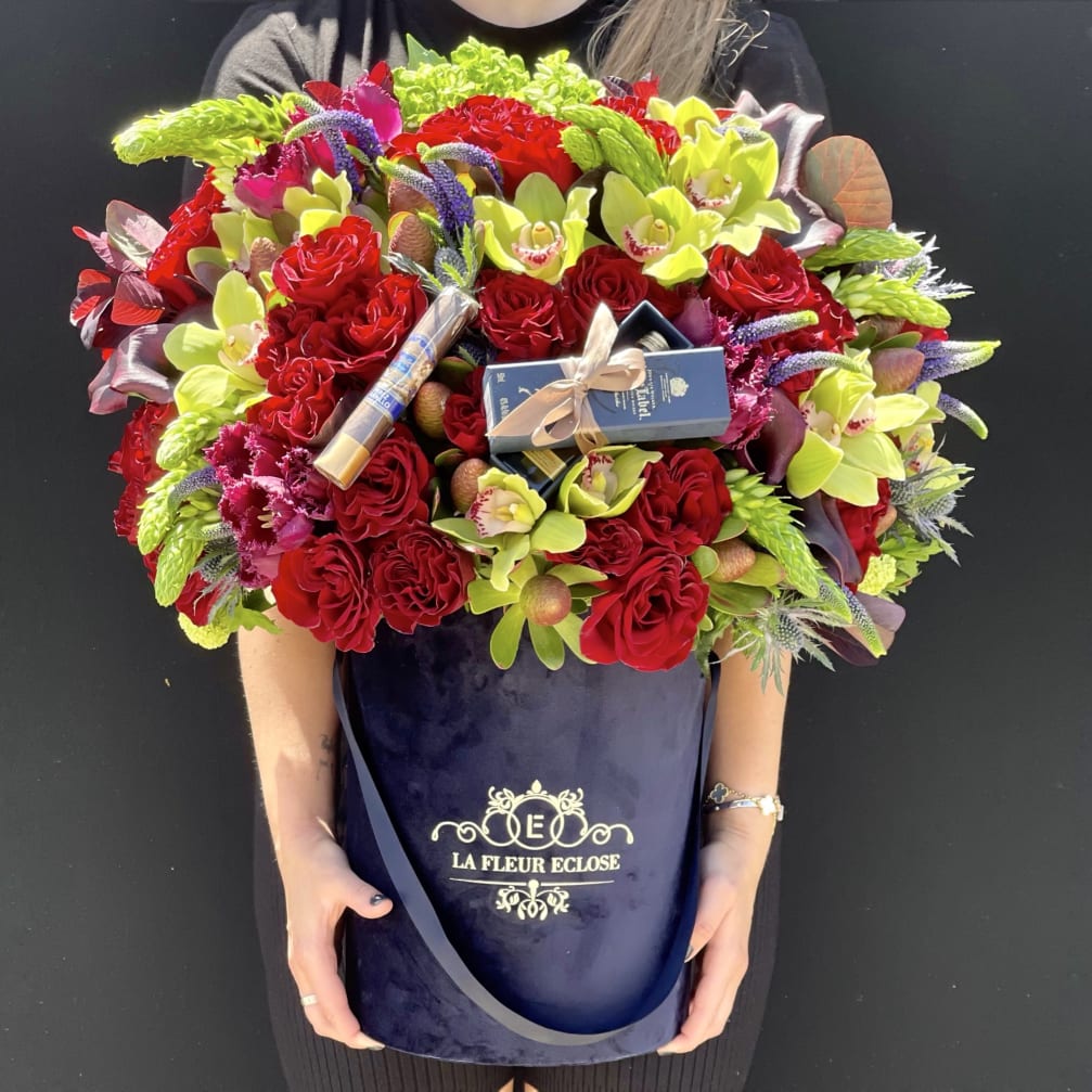 Large bouquet of red roses and lime-green orchids in a navy hatbox with chocolates