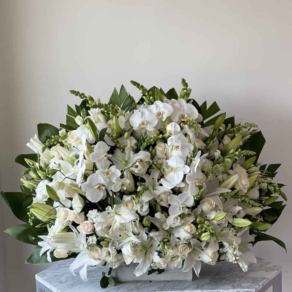 Large white floral arrangement with orchids and lilies in a low container